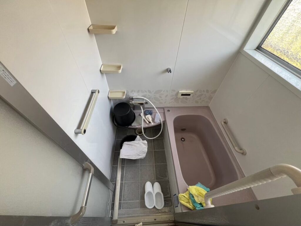 施工前、浴室を入口側から見たところ。右に紫がかったピンクグレーの浴槽、奥にカウンター、床は濃いグレーのタイル