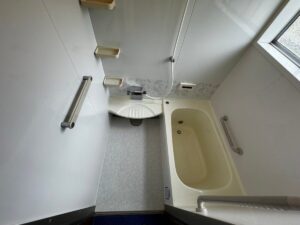 施工後、最初の施工前と同じ位置から見た浴室。ライトアイボリーの浴槽とカウンター、明るいグレーの床シート