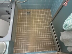 施工前、タイル張りの浴室を入口側から見たところ。床は茶色がかったグレーの小さな角タイル