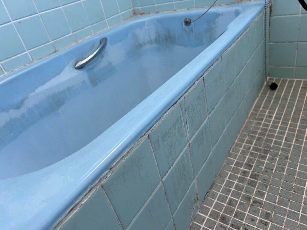 施工前、水色のホーロー浴槽を横から見たところ。浴槽まわりのタイルと、床のモザイクタイル