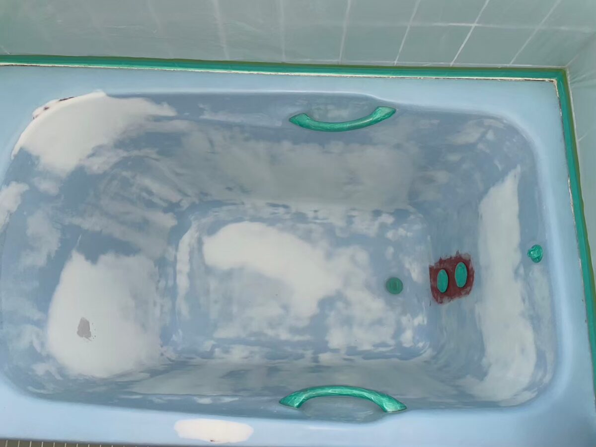 施工の途中。浴槽のまわりを緑のテープで養生し、表面に白っぽい部分がまだらに見える