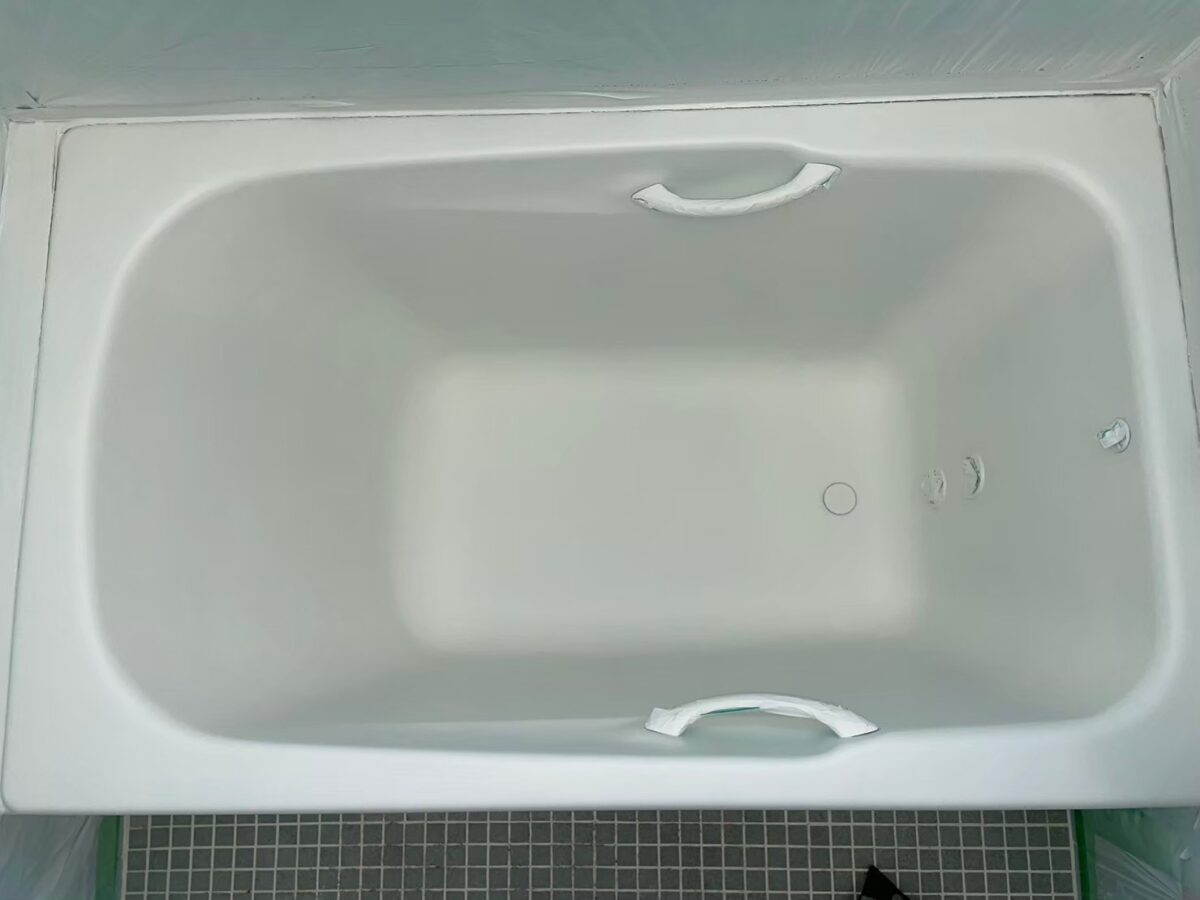 施工の途中、ベースコートを吹き付けた浴槽。白くつやのない状態で、取っ手にテープを貼っている