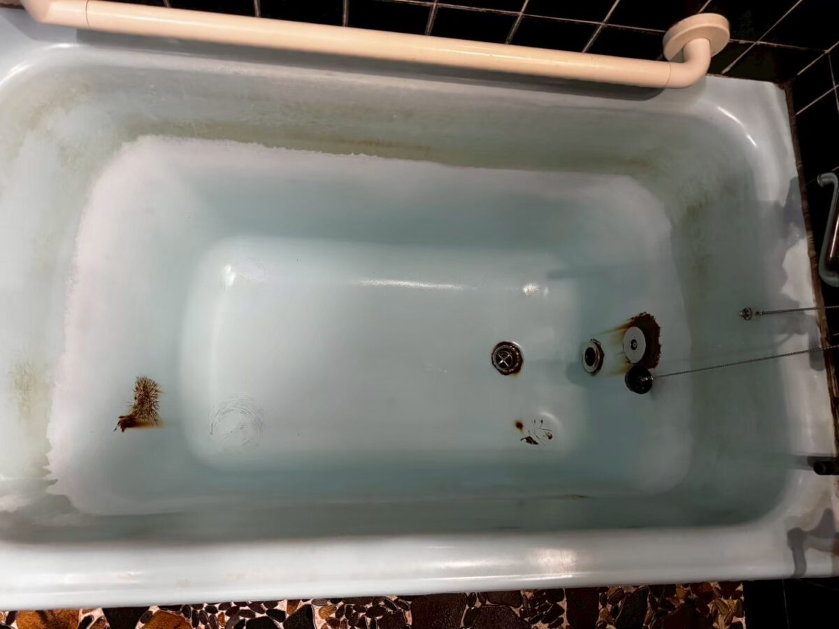 施工前、浴槽の内側を上から見たところ。金具のまわりにサビ色の汚れ、底にサビ色の点がある