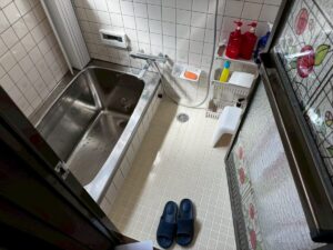 施工前、浴室を入口側から見たところ。左にステンレス浴槽、床はクリーム色の小さなタイル、右に濃い茶色の枠のドア