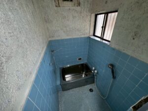 施工前、浴室の入口から見たところ。青いタイルの壁と凹凸のある壁、奥に浴槽がある