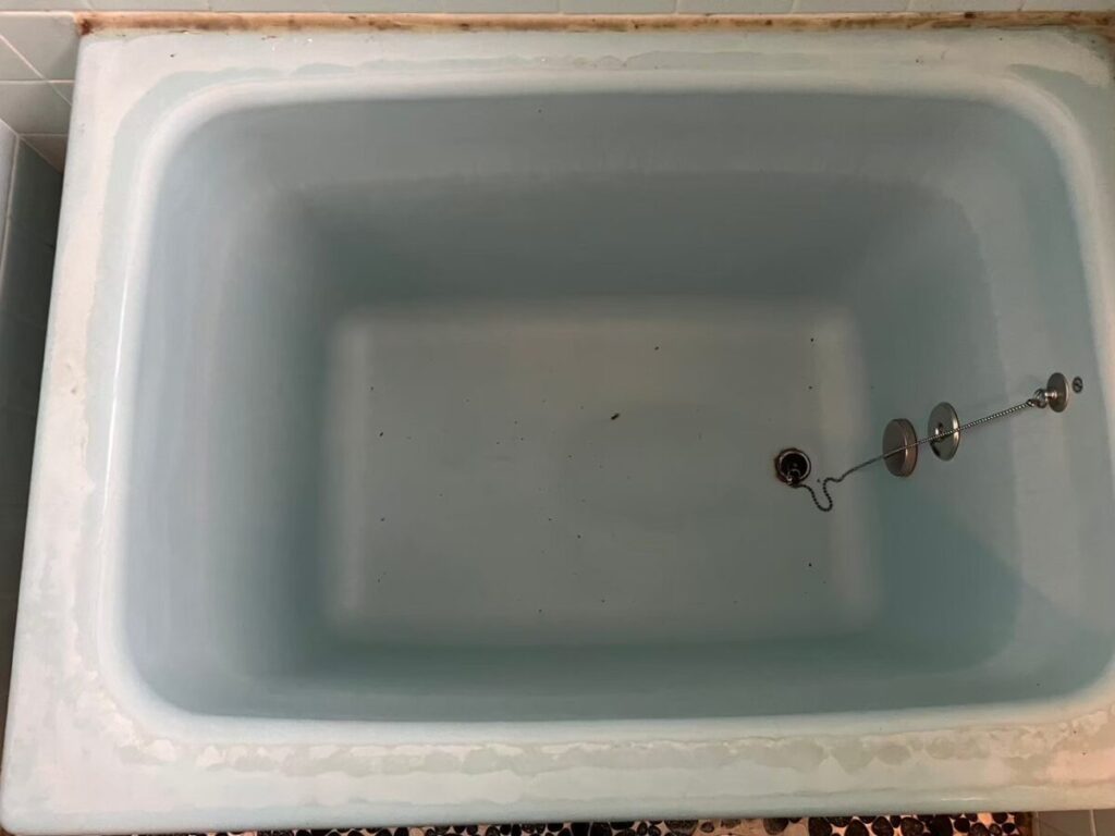 施工前、水色のホーロー浴槽を真上から見たところ。ふちに白っぽい汚れがあり、底に黒い点状の汚れが散らばっている