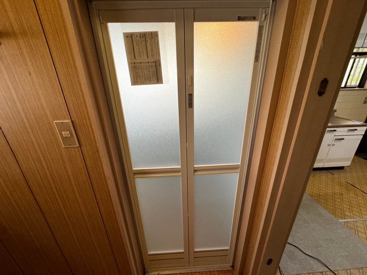 施工後、交換した浴室ドアを脱衣所側から見たところ。白いフレームに半透明のパネルの折れ戸