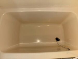 和泉市の施工前、ユニットバスの浴槽を真上から見たところ。内側は黄みがかったクリーム色で、排水口にチェーンのついた栓がある