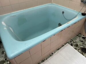 施工前、水色のホーロー浴槽を斜め前から見たところ。右のふちの塗装がはがれ、左の壁に白っぽいものが筋のように残っている