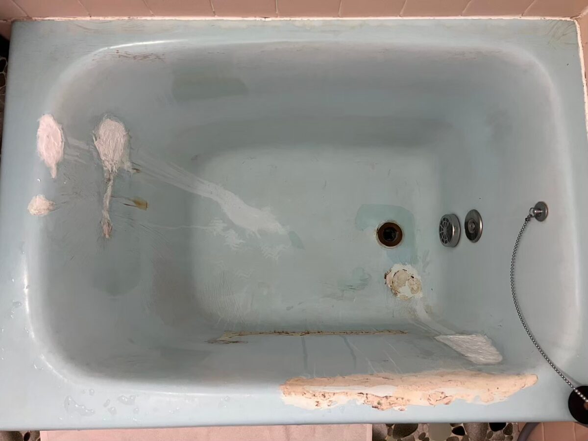 施工前、浴槽の内側を真上から見たところ。左の壁に白っぽい盛りつけ、排水口のそばと手前のふちに肌色の盛りつけがある