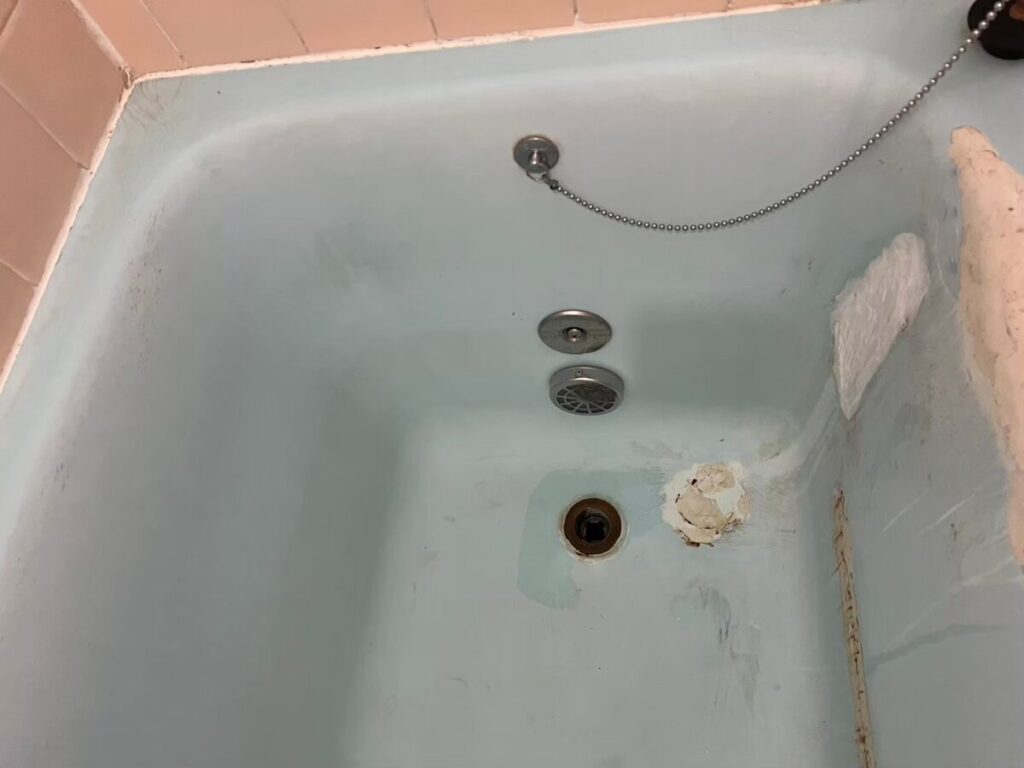 施工前、浴槽の内側を排水口の側から見たところ。排水口のそばに肌色の盛りつけがあり、右の壁にも白っぽい盛りつけがある
