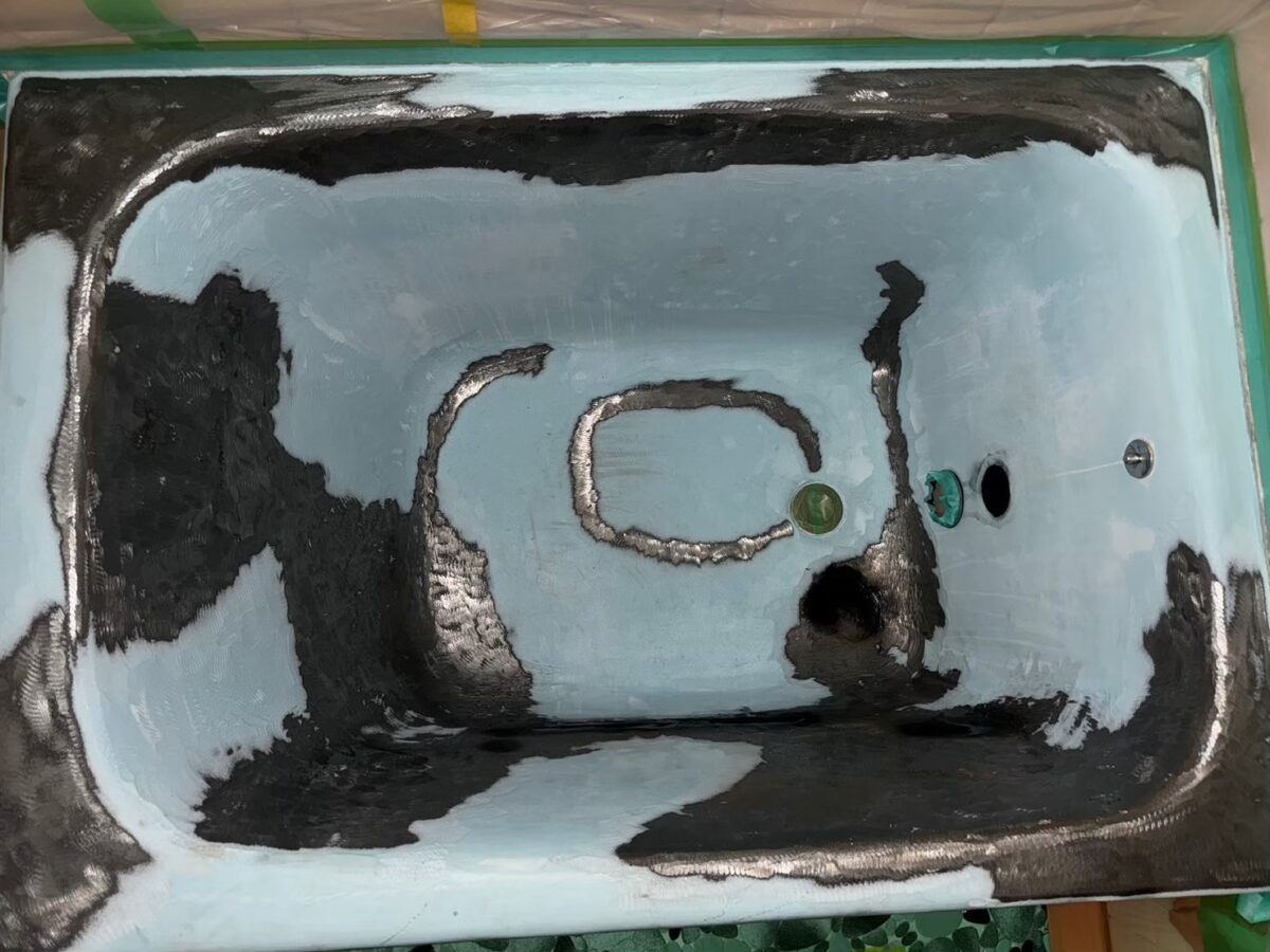 工事の途中、浴槽のまわりを緑のテープで養生した状態。内側の水色の面に黒く光る部分がまだらに広がっている