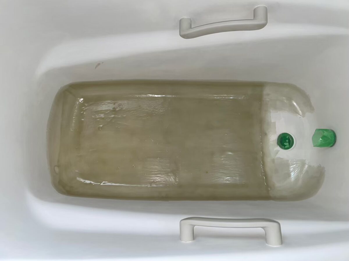 浴槽の底に補強用の材料を塗り広げている工程(排水口は緑のキャップで保護)