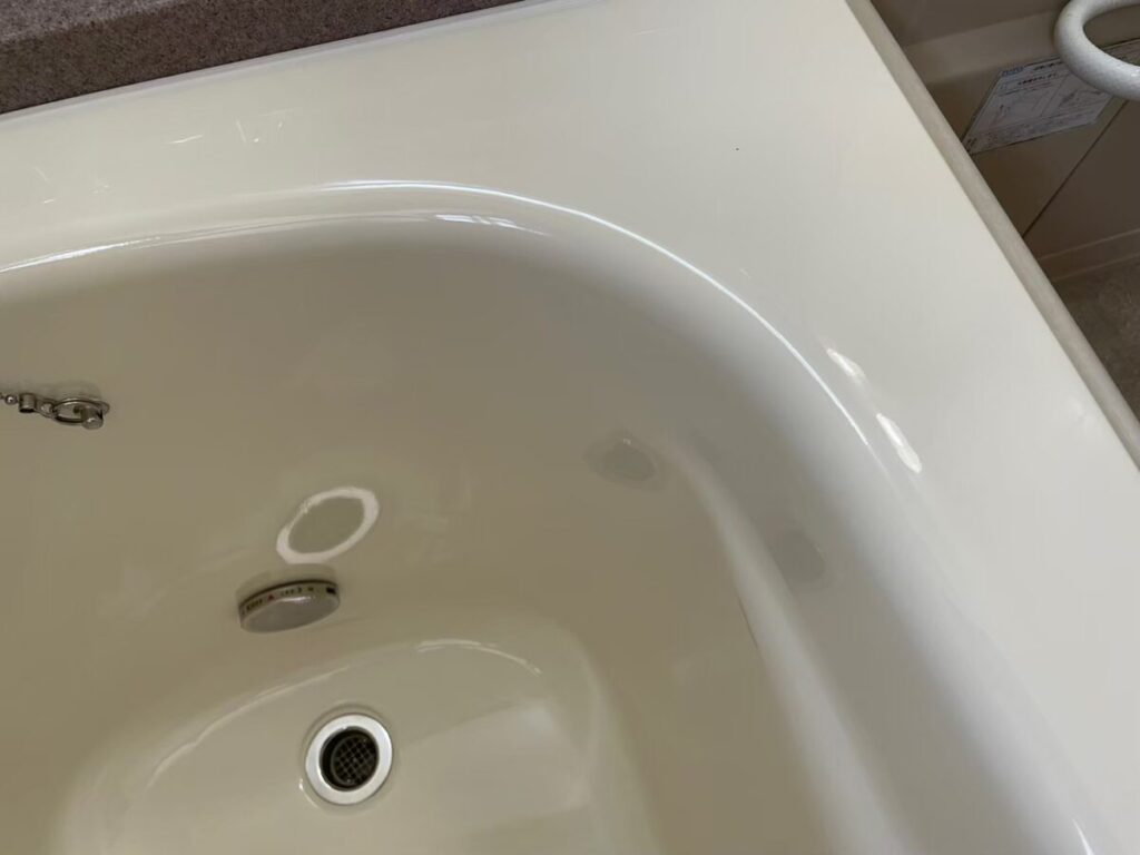 施工後、浴槽のふちから見下ろした排水口とオーバーフローのまわり。内側がつやのあるライトアイボリーになっている