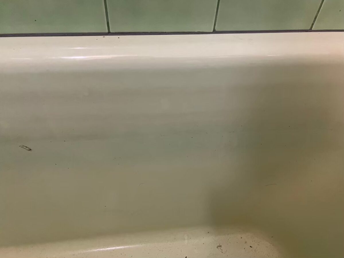 施工前、浴槽のふちの内側。水面の高さに沿って緑がかった帯状の汚れが重なっている