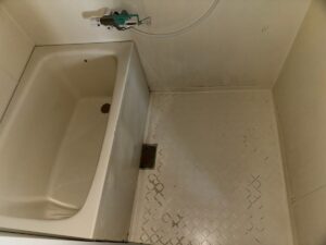 施工前、賃貸ユニットバスを入口の側から見たところ。左に浴槽、右の洗い場の床は白い菱形の模様がまだらに欠けている