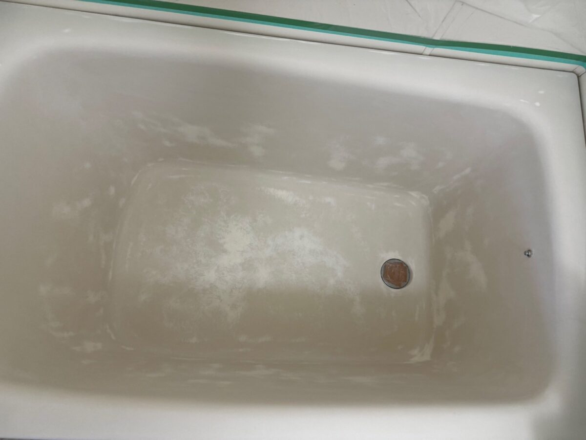 工程、浴槽の内側が白っぽいまだら模様になっている。ふちは緑のテープで養生している