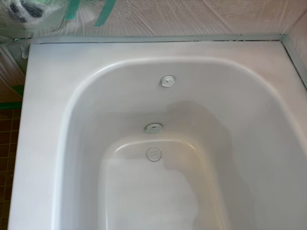 工程の途中、浴槽の内側が白くつや消しの面になっている。ふちのまわりは緑のテープとビニールで養生している