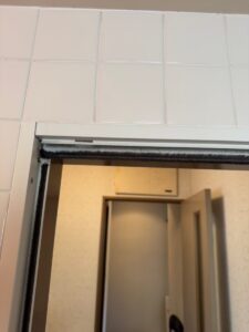 施工前、浴室の中から入口を見たところ。ドアの上のレールに黒い汚れがあり、奥に脱衣所が見える