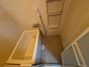 施工前、賃貸ユニットバスを入口側から見たところ。左に黄みがかった浴槽、右に茶色っぽい樹脂の洗い場の床と折れ戸が見える