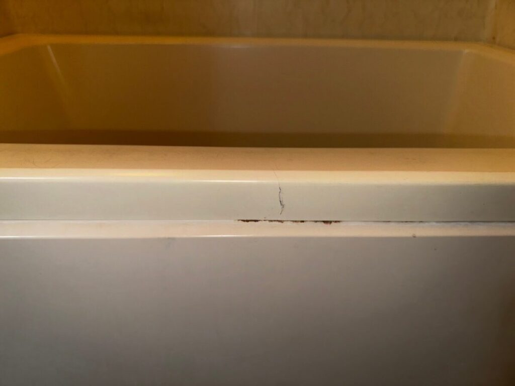 施工前、浴槽のふち(フランジ)の合わせ目を正面から見たところ。細い亀裂が1本あり、合わせ目に沿って黒っぽい汚れが付いている