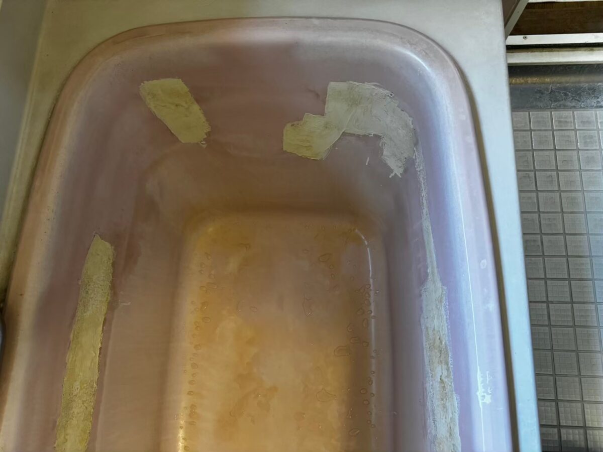 施工前、浴槽の端の角。ピンク色の面に黄色っぽい帯状のものと白っぽい膜状のものが貼りついている