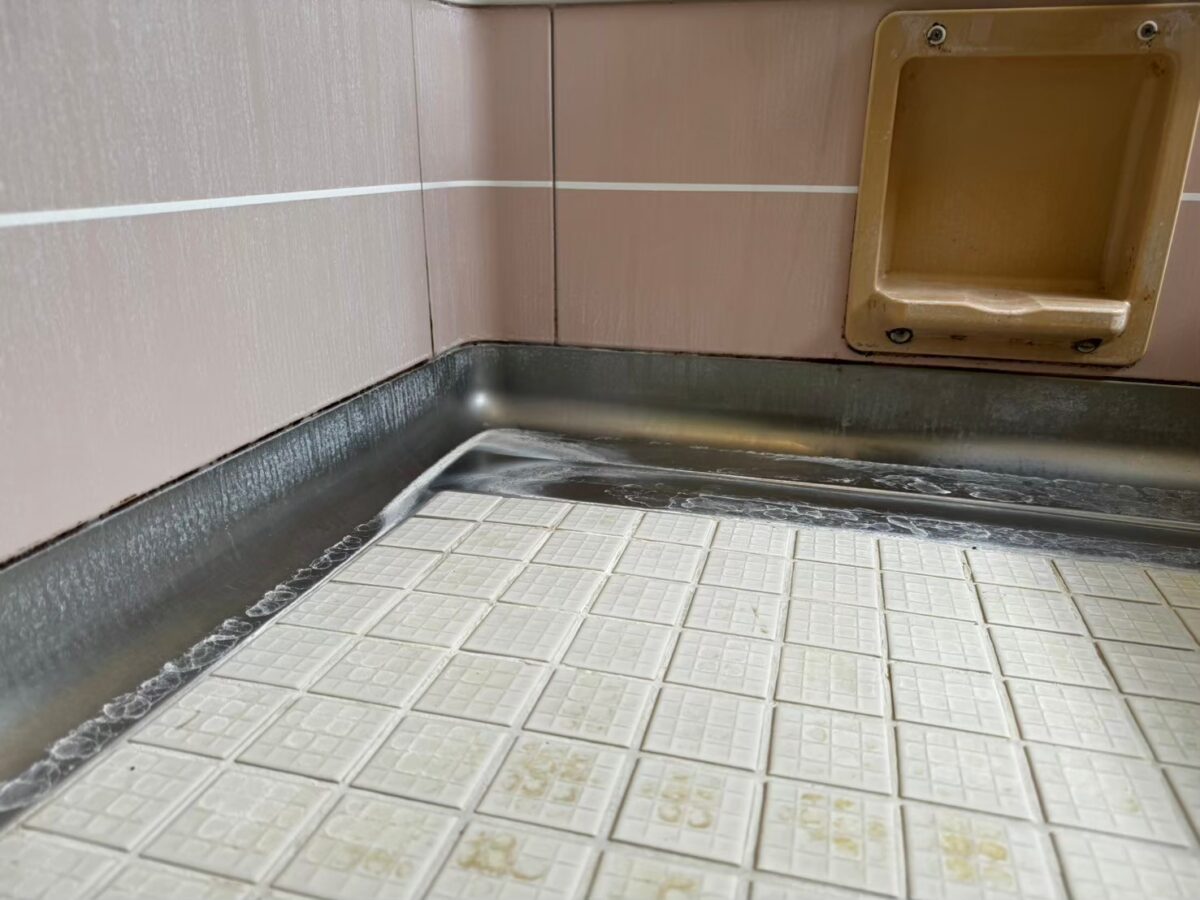 施工前、壁の小物入れのある隅。金属の立ち上がりのふちに白い筋状の汚れがある
