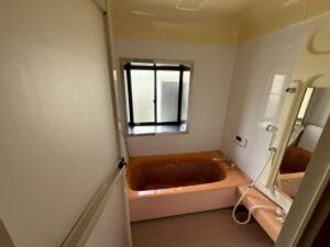 施工前、浴室を入口側から見たところ。奥に窓と、オレンジがかったピンク色の浴槽がある