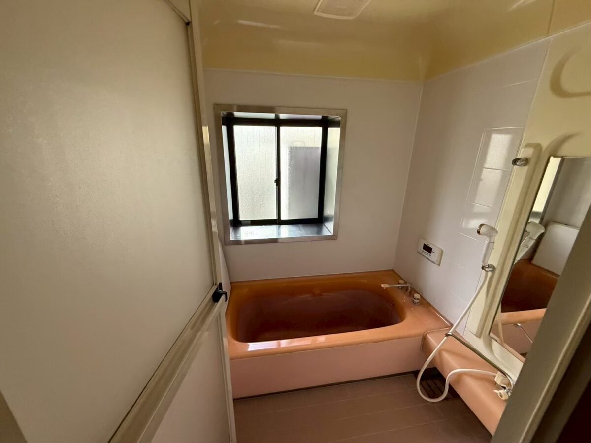 施工前、浴室を入口側から見たところ。奥に窓と、オレンジがかったピンク色の浴槽がある
