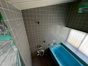施工前、養生をした在来浴室を入口側から見たところ。グレー系のタイルの壁と水色の浴槽