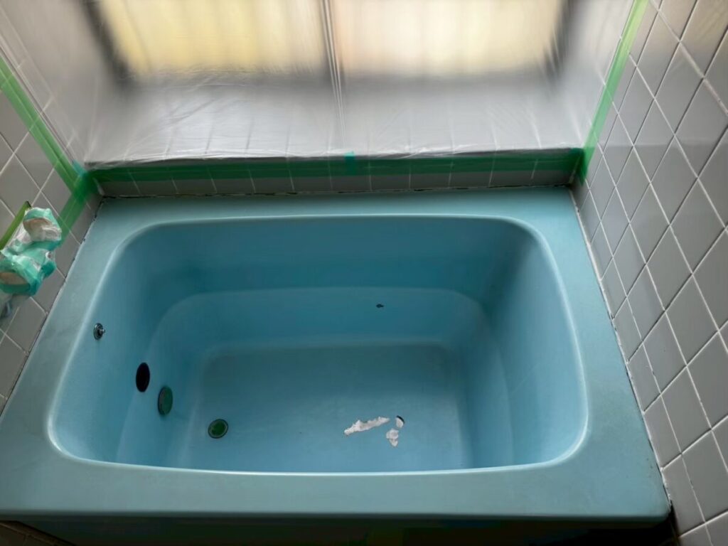 施工前、水色の浴槽を前から見下ろしたところ。底に白っぽくはがれた跡がある