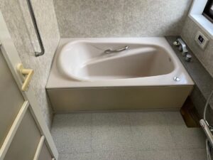 施工前、浴室を入口側から見たところ。奥に淡いピンクベージュの浴槽があり、左にドアと手すりが見える