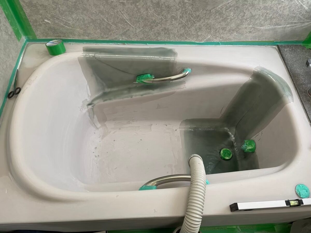 工程の途中、浴槽のまわりを緑のテープとビニールで養生した様子。内側の一部が濃い灰緑色になっている
