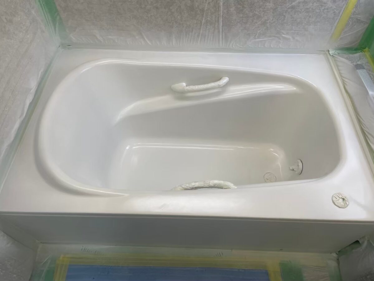 工程の途中、浴槽の内側全体が白くなった状態。手すりと排水口に白い養生が残っている