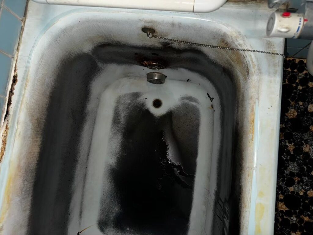 施工前、水栓側から浴槽の内側を見たところ。底から壁にかけて黒い汚れが広がっている