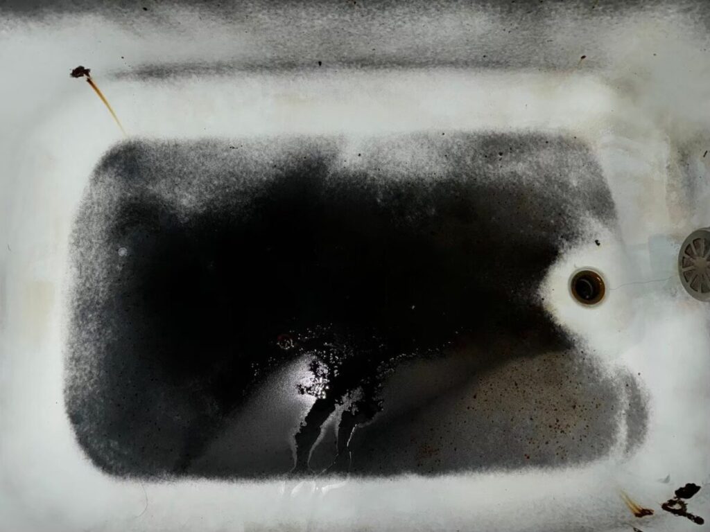 施工前、浴槽の内側の底を真上から見たところ。底の大部分が黒く、サビ色の小さな汚れが点々とある