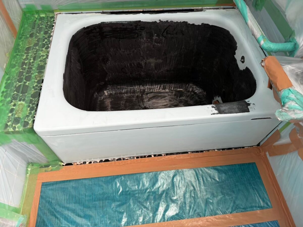 工事の途中、浴槽のまわりをテープとビニールで養生した状態。浴槽の内側は黒く、前面は白っぽい