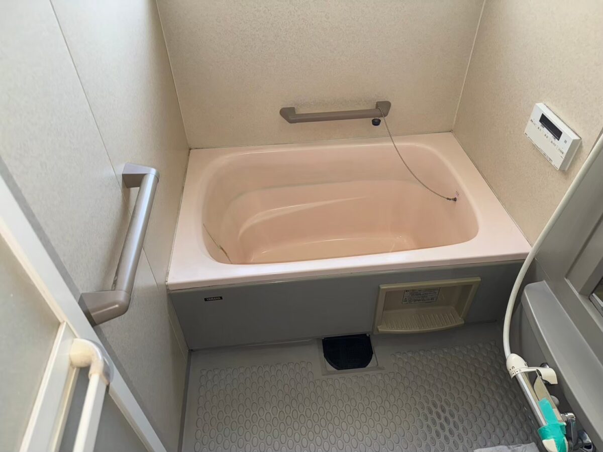 横浜市旭区の施工前、ユニットバスのピンク色の浴槽。壁に手すりとリモコンがある
