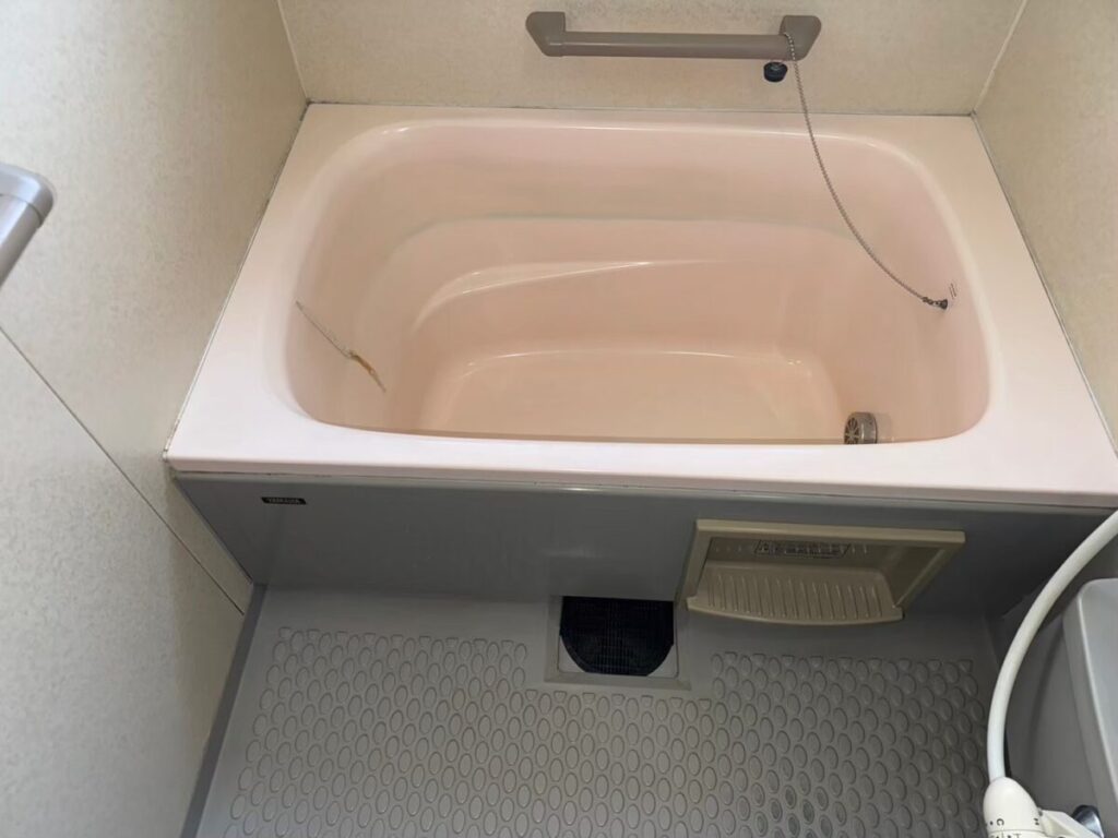 施工前、ピンク色の浴槽を正面から見たところ。内側の左側に細い茶色い線のようなひび割れが見える