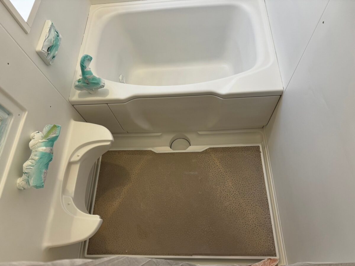 工程、浴槽・腰掛け・壁が白くなった状態。水栓まわりには養生が残り、床は茶色い粒状の模様のまま
