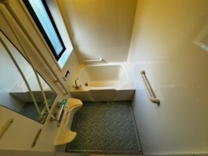 施工後、同じ角度から見た浴室。浴槽と壁が明るくなり、床は青緑がかったグレーのモザイク柄の床シートになっている
